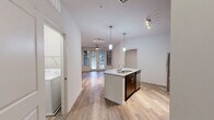 Located at 1100 South Blvd in Charlotte's vibrant South End neighborhood, this one-bedroom, one-bathroom unit offers a well-designed open-concept layout across a single floor. The combined living, dining, and kitchen area serves as the heart of the home, anchored by a curved granite-topped island with an undermount sink and elegant pendant lighting overhead. The kitchen is outfitted with rich dark cabinetry, granite countertops, a subway tile backsplash, and a full suite of stainless steel appliances including a refrigerator, range, and microwave. Light wood-tone flooring runs throughout the main living areas, complemented by ceiling fans and a wall of French doors that invite natural light into the living room. The bedroom features plush carpet, a ceiling fan, and a window with outdoor views, along with access to a spacious walk-in closet equipped with wire shelving. The bathroom includes a tiled tub-shower combination, a dark-cabinet vanity with a granite countertop, and matching wood-tone flooring. A dedicated laundry area accommodates a full-sized washer. Additional closet and utility spaces round out this efficiently planned and thoughtfully finished home.