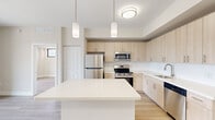 Located at 8400 NW 27th Ave in Miami, FL, this modern single-floor residence offers three bedrooms, two bathrooms, a living room, and a well-appointed kitchen. The open-concept kitchen is a standout feature, showcasing light wood cabinetry that extends floor to ceiling, a large white quartz island with pendant lighting, stainless steel appliances including a refrigerator, range, microwave, and dishwasher, and a clean white backsplash that enhances the bright, airy aesthetic. Light wood-toned luxury flooring flows consistently throughout the unit, reinforcing the cohesive contemporary design. The bedrooms are bright and neutral-toned, with large black-framed windows that invite natural light. Select bedrooms feature sliding glass doors opening to private balconies with outdoor views of the surrounding Miami neighborhood. The bathrooms are finished with elegant marble-style tile surrounds in the tub-shower combination, complemented by brushed gold fixtures and matching tile flooring. A dedicated hallway and closet provide practical storage solutions. The overall ambiance is clean, modern, and functional, with a consistent neutral palette and contemporary finishes throughout that create a welcoming and livable environment.