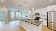 Located at 1020 Port Royal Trail in Myrtle Beach, SC, this thoughtfully designed single-floor residence offers a clean, modern aesthetic throughout. The open-concept living area seamlessly connects the kitchen, dining, and living spaces, creating an airy and functional layout bathed in natural light from large windows with white blinds.

The kitchen is a standout feature, anchored by a generous island with a dark quartz countertop, undermount sink, and matte black faucet. Elegant pendant lights hang above the island, complementing the full suite of stainless steel appliances — including a range, microwave, and refrigerator. Crisp white shaker cabinetry with black hardware and a subway tile backsplash complete the polished look. A dedicated pantry adds practical storage.

Light hardwood flooring runs throughout the unit, enhancing the bright, cohesive feel. The living area features crown molding and a ceiling fan, while recessed lighting provides consistent illumination across the open floor plan.

The bedroom is a comfortable, well-proportioned retreat with a ceiling fan, natural light from a large window, and two closets. The bathroom features a white tub-shower combo with clean tile surround, white cabinetry with a dark countertop, and matte black hardware and accessories. A dedicated laundry area rounds out the home's practical amenities.