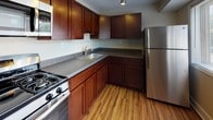 This single-floor residence offers a thoughtfully designed layout that balances comfort and functionality. The open living area is generously proportioned, featuring warm beige carpeting, clean white walls with classic crown molding, and a large sliding glass door dressed with vertical blinds that fills the room with natural light. The space flows naturally through the unit, connecting seamlessly to the other areas.

The kitchen is a standout feature, showcasing rich dark wood cabinetry paired with dark granite-style countertops and warm wood-look flooring. Stainless steel appliances, including a refrigerator and a gas range, complete the modern and practical cooking space, making it both attractive and highly functional.

The bedroom is a quiet retreat with plush neutral carpeting and a window offering views of the surrounding exterior, allowing for natural light and ventilation. A closet with a paneled door provides ample storage.

The bathroom is finished with clean white square tile surrounding a full soaking tub with shower, complemented by a light countertop vanity with dark wood cabinetry below, creating a crisp and tidy aesthetic. Throughout the residence, the neutral color palette and consistent finishes create a cohesive and inviting atmosphere.