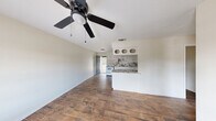This single-story, 2-bedroom, 1-bathroom home offers a practical and cohesive layout with consistent wood-look flooring carried throughout every room. The open-concept living area flows seamlessly into the kitchen, which is equipped with white cabinetry featuring decorative open upper shelving, a striking marble-look backsplash and countertops, a white range, and a full-size refrigerator — all anchored by a peninsula that separates the kitchen from the living space. A ceiling fan with a light fixture keeps the living area comfortable, while a teal-accented front door adds a subtle design detail. Both bedrooms are well-proportioned, with the primary bedroom offering ample space, and each room includes a ceiling fan, natural light from a dedicated window, and a built-in closet with a hanging rod for storage. The bathroom is cleanly finished with a marble-look vanity, a tub-shower combination featuring textured white tile surround, and matching flooring. A dedicated utility room rounds out the layout, adding practical functionality. The neutral color palette and cohesive finishes throughout give the home a clean, move-in-ready feel.