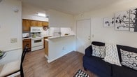 This single-floor residence offers a thoughtfully arranged layout that balances comfort and functionality throughout its key living spaces. The living area is bright and welcoming, featuring warm hardwood-style flooring, a textured ceiling, and a full-length sliding glass door dressed with vertical blinds that opens to an outdoor patio, allowing natural light to fill the room and providing direct access to the exterior. The open-concept kitchen is efficiently designed with warm wood cabinetry, white appliances including a range and built-in microwave, and a raised breakfast bar that connects the kitchen to the living and dining area — ideal for casual meals or entertaining. The bedroom is a serene retreat, carpeted for comfort, and equipped with a ceiling fan with integrated lighting and a dedicated closet for ample storage. The bathroom is clean and practical, featuring a tiled tub-shower combination with a curtain, a toilet, and an overhead wood-toned wall cabinet that provides additional storage. The consistent use of neutral tones, hardwood-style floors in the main living areas, and carpet in the bedroom creates a cohesive and comfortable ambiance throughout this well-designed residence.