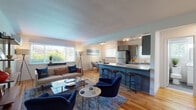 Located at 41 Wolfpit Ave in Norwalk, Connecticut, this single-floor residence offers a thoughtfully designed open-concept layout with warm hardwood flooring flowing seamlessly throughout. The living area is generously sized, filled with natural light from large windows, and anchored by a comfortable seating arrangement alongside a wall-mounted television and mid-century-inspired shelving. A peninsula with granite countertops and bar seating connects the living space to the kitchen, which is outfitted with sage-toned shaker cabinets, a white subway tile backsplash, granite countertops, and stainless steel appliances including a gas range with microwave. A dedicated dining nook accommodates a glass-top round table and provides a bright, tree-lined window view. The primary bedroom features a bold navy accent wall, a built-in closet, a wall-mounted mini-split unit, and ample room for a workspace. A second bedroom is bright and serene with neutral tones and garden views. The bathroom is finished with slate-style tile flooring, a white vanity with under-cabinet storage, and a tub-shower combination. The space combines contemporary finishes with a cohesive coastal-inspired color palette, creating a welcoming and functional living environment.
