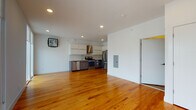 This single-floor unit offers a clean, modern aesthetic defined by warm-toned hardwood flooring that flows seamlessly throughout the entire space. The open-plan layout connects the living area to the kitchen, creating a bright and airy atmosphere enhanced by recessed ceiling lighting.

The kitchen is well-appointed with a full suite of stainless steel appliances, including a gas range, dishwasher, and French door refrigerator. White upper cabinetry is paired with dark lower cabinets, complemented by a tile backsplash and a dedicated stainless steel range hood. Ample counter space and storage make this kitchen as functional as it is stylish.

The living area is generously proportioned and benefits from large sliding glass doors that open onto a private outdoor balcony, flooding the interior with natural light and offering views of the surrounding neighborhood. The white walls and smooth ceilings contribute to the space's clean, contemporary feel.

The bathroom features wood-look tile flooring, white tile walls, and a combined shower and soaking tub with modern brushed-nickel fixtures, maintaining the refined, minimalist style found throughout the unit. Additional features include a utility panel and closet storage, rounding out a well-designed and functional living space.