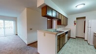 Located at 2 Northridge Terrace in Madison, WI, this single-floor unit offers a practical and functional layout designed for comfortable everyday living. The open-concept design connects the kitchen and living area seamlessly, creating a spacious, cohesive feel throughout the main living space.

The kitchen is a standout feature, equipped with a galley-style configuration that maximizes storage and workspace. Warm-toned wood cabinetry lines both upper and lower sections, complemented by light countertops and a peninsula that doubles as a workspace and casual dining area. The peninsula houses a double-basin sink and provides a natural visual divider between the kitchen and living room. Tile flooring in the kitchen adds durability and easy maintenance, while a full suite of appliances — including a refrigerator, electric range, and dishwasher — ensures everyday convenience.

The living area is generously proportioned, featuring plush carpeting, a ceiling fan, and a wall-mounted HVAC unit. A sliding glass door floods the room with natural light and provides direct access to an outdoor area. A hallway leads to additional rooms, including a carpeted bedroom with a spacious walk-in closet offering built-in shelving and hanging space, alongside a vanity area with wood cabinetry and a mirror.
