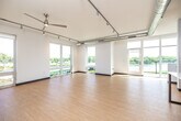 This contemporary single-floor space showcases a clean, modern design with an open layout that maximizes natural light and outdoor views. Light wood-tone flooring runs consistently throughout, complemented by crisp white walls and bold navy blue baseboards that add a distinctive finishing touch.

The expansive main living area is defined by large floor-to-ceiling windows and glass doors that frame sweeping views of a river, bridge, and surrounding greenery. Exposed silver ductwork runs along the ceiling alongside track lighting, lending an industrial-modern character to the space. A ceiling fan adds both function and style.

The kitchen is thoughtfully designed with light wood cabinetry, a white countertop island, a subway tile backsplash, and a full suite of stainless steel appliances including a refrigerator, dishwasher, range, and microwave. Pendant lighting above the island enhances the kitchen's contemporary aesthetic.

The bedroom offers a generous walk-in closet with a sliding wood panel door, exposed ductwork, and a large window that fills the room with natural light. An additional room with track lighting and a floor-to-ceiling window provides flexible use as an office or studio space.

The bathroom features warm wood cabinetry, a white countertop with an undermount sink, a full bathtub, and clean, minimal finishes throughout. The overall ambiance is bright, airy, and modern.