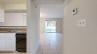 Located at 349 Scottsdale Square in Winter Park, FL, this one-bedroom, one-bathroom unit offers a practical and well-organized single-floor layout. Light-colored ceramic tile flooring runs consistently throughout all rooms, creating a cohesive and easy-to-maintain interior. The combined living and dining area forms the heart of the unit, with the living room anchored by a sliding glass door that floods the space with natural light and provides views of a lush green outdoor area. The dining area features a multi-bulb chandelier overhead, adding a modest decorative touch. The kitchen is equipped with white cabinetry, granite-style countertops, and a white electric range, with a window allowing additional natural light. A hallway connects the main living areas to the private quarters. The bedroom offers a comfortable footprint with a double-door louvered closet, a window with blinds, and the same tile flooring found throughout. The bathroom includes a full-size tub and shower combination with chrome fixtures. Textured ceilings are present throughout the unit, and the neutral wall tones contribute to a clean, bright ambiance well-suited to the sunny Winter Park climate.