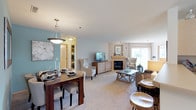 This single-floor residence offers a thoughtfully designed layout that balances comfort and functionality across its key living areas. The open-plan living and dining space is immediately welcoming, featuring soft carpet flooring, neutral tones, and a standout teal accent wall in the dining area. A pendant light fixture anchors the dining space, which comfortably accommodates a full dining table and chairs. The living room centers around a tiled fireplace flanked by a sliding glass door that invites natural light and outdoor views, creating a bright and airy atmosphere.

The kitchen is efficiently laid out with light wood cabinetry, white appliances including a refrigerator, stove, and over-range microwave, and a peninsula counter with bar seating. A breakfast nook with a window provides an additional casual dining option.

The primary bedroom is a serene retreat, featuring multiple windows with garden views, plush carpet, and elegant drapery. The second bedroom offers flexible use with ample natural light and carpeted flooring. Both bathrooms are finished with light wood vanity cabinetry, white countertops, and tile flooring. A shared hallway connects the sleeping quarters to the main living areas, completing this cohesive and comfortable residence.