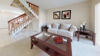 This two-floor residence is thoughtfully laid out across two distinct levels, each designed to serve specific living functions. The main level features light-tiled flooring throughout the dining and kitchen areas, creating a clean, cohesive aesthetic. The dining area accommodates a round table for four beneath a ceiling fan, and benefits from natural light through a window. Adjacent to the dining space, the galley-style kitchen is equipped with white appliances including a range, dishwasher, microwave, and refrigerator, complemented by wood-trimmed cabinetry offering ample storage.

The living room on the main level is carpeted and centers around a tiled fireplace flanked by large sliding glass doors that allow generous natural light and outdoor views. Track lighting overhead adds a practical, modern touch. A staircase with a warm wood banister connects the main level to the upper floor.

Upstairs, plush carpeting extends through the bedroom area, which offers a comfortable and quiet retreat. The primary bedroom is generously sized, featuring a bright window, ample floor space, and direct access to an en-suite bathroom equipped with a shower. The upper level's open layout and proximity to the staircase landing contribute to an airy, connected feel throughout the home.
