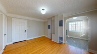 Located at 2209 NW Everett St in Portland, Oregon, this single-floor unit offers a thoughtfully laid-out interior with a blend of classic architectural details and functional design. The main living area greets you with warm hardwood floors, neutral painted walls, and a textured ceiling, with a wall-mounted heating unit providing efficient climate control. An elegant arched doorway connects the living space to adjoining rooms, adding a timeless architectural touch. The bedrooms continue the hardwood flooring and feature generous closet storage, including built-in cabinetry painted in a soft blue-gray, maximizing organization and utility. Natural light filters through windows fitted with blinds, creating a bright and comfortable atmosphere. The bathroom is a standout feature, showcasing classic white subway tile wrapping the tub surround, a window for natural ventilation, a pedestal sink, and a distinctive black-and-white hexagonal mosaic tile floor — a nod to vintage charm. The kitchen is well-equipped with gray shaker-style cabinetry, open shelving, a stainless steel refrigerator, and striking patterned encaustic-style tile flooring, lending the space a stylish and functional character. Overall, the unit presents a cohesive aesthetic that balances classic detailing with practical living in one of Portland's desirable northwest neighborhoods.