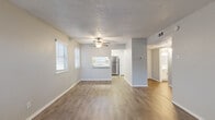 This efficient and thoughtfully designed single-floor residence offers a functional layout across five distinct spaces: a combined kitchen and living room, one bedroom, a hallway, a bathroom, and a closet. The open-concept living area is finished with light wood-look vinyl flooring and neutral gray walls, creating a clean, contemporary aesthetic. A ceiling fan provides added comfort, while multiple windows fitted with blinds invite natural light throughout the space. The kitchen connects seamlessly to the living area via a pass-through counter with a white quartz surface, and is equipped with white cabinetry, a stainless steel refrigerator, and additional natural light from a dedicated window. A hallway leads to the private bedroom, which features plush carpeting, a window for natural light, and access to a dedicated closet — offering a comfortable and well-sized retreat. The full bathroom is clean and simply designed, featuring wood-look tile flooring, a tub-shower combination with white tile surround, and a vanity. Throughout the unit, textured ceilings and consistent neutral tones lend a cohesive and move-in-ready feel to the overall space.