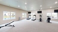Located at 693 Morsani Pl in Tontitown, Arkansas, this dedicated exercise room offers a generously sized, single-floor fitness space designed for a comprehensive workout experience. The room features neutral-toned walls and plush wall-to-wall carpeting that provides a clean, comfortable foundation for a wide range of exercises. Recessed lighting is distributed evenly across the smooth ceiling, ensuring bright, consistent illumination throughout the space. Multiple ceiling-mounted flat-screen televisions are positioned for easy viewing from various workout stations, enhancing the exercise experience. A series of large windows lines the walls, inviting abundant natural light and providing views of the surrounding outdoor area, including what appears to be a patio and neighboring grounds. The layout accommodates a variety of equipment, including treadmills, an elliptical, a stationary bike, a multi-function cable machine, a weight bench, and a dumbbell rack, allowing for both cardio and strength training. A large wall mirror further opens up the space and supports form-focused training. Two interior doors provide convenient access to adjoining areas. The overall ambiance is modern, clean, and functional, making this a well-appointed space for dedicated fitness use.