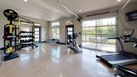 Located at 12007 E Coyote Rock Dr in Spokane Valley, WA, this fitness center offers a thoughtfully designed, single-level workout facility built to support a comprehensive exercise experience. The space is defined by its gleaming polished terrazzo floors, which reflect generous natural light streaming in through clerestory windows and large glass garage-style doors that open directly to an outdoor patio area, creating a seamless indoor-outdoor connection with views of the surrounding landscape.

The open floor plan provides ample room for a wide variety of cardio and strength training equipment, including treadmills, a stationary bike, an elliptical, a rowing machine, and a WaterRower. A multi-functional strength rack is outfitted with TRX suspension trainers, medicine balls, kettlebells, and weight plates, catering to diverse fitness routines. Full-length wall mirrors enhance the sense of openness while allowing users to monitor their form. A wall-mounted television is positioned for visibility across the cardio area.

Recessed lighting throughout the ceiling supplements the natural light, ensuring a bright and energizing atmosphere. Modern dark-framed doors with frosted glass panels add a refined architectural detail, while a dedicated restroom is accessible within the space. The overall ambiance is clean, contemporary, and highly functional, making this fitness center a standout amenity.