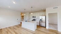 This single-story home offers a thoughtfully designed layout encompassing 3 bedrooms, 2 bathrooms, a utility room, and a dedicated closet. The open-concept kitchen and living area forms the heart of the home, showcasing light hardwood-style flooring, neutral warm-toned walls, and abundant natural light streaming through multiple windows with blinds. The kitchen is outfitted with crisp white shaker cabinetry, a classic subway tile backsplash, stainless steel appliances including a gas range, microwave, and French door refrigerator, and a central island with a built-in sink and light quartz countertops, illuminated by stylish globe pendant lights. The spacious living area features a ceiling fan and multiple windows offering outdoor views, creating an airy, open atmosphere. Each bedroom is carpeted, finished in soft neutral tones, and equipped with a ceiling fan, with windows providing natural light and exterior views. The primary bedroom includes a dedicated walk-in closet with wire shelving for organized storage. The bathrooms are clean and modern, featuring white cabinetry, quartz countertops, and hardwood-style flooring, with one bathroom offering a full tub-shower combination. A utility room and hallway complete this practical and welcoming home.