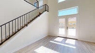 This well-designed two-story home offers a clean, contemporary aesthetic defined by neutral tones, light wood flooring, and an abundance of natural light. The main living area makes an immediate impression with its dramatic double-height ceiling and elegant staircase featuring wrought iron balusters. A set of white French doors topped with a transom window floods the space with sunlight and provides views of the surrounding neighborhood. The open-concept kitchen is outfitted with slate-blue shaker cabinetry, a white peninsula countertop, and stainless steel appliances including a refrigerator, microwave, and range. The layout connects seamlessly to adjacent living areas, creating a cohesive flow throughout the ground floor. Additional rooms on the main level include a bright secondary space with French doors, a ceiling fan, and generous natural light. A full bathroom with a soaking tub and a stacked washer and dryer unit offer convenient in-unit laundry. Upstairs, a spacious loft-style area with an open railing overlooks the lower level, further enhancing the sense of vertical space. Bedrooms feature light-filled windows with blinds and clean, understated finishes. Throughout, consistent light wood flooring and crisp white walls create a bright, move-in ready environment.