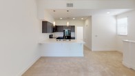 Located at 1257 Armorlite in San Marcos, unit #124 is a single-floor residence designed with a clean, contemporary aesthetic throughout. The open-concept layout connects the living area to a well-appointed kitchen, creating a cohesive and functional living space. The kitchen is a standout feature, showcasing dark espresso-toned cabinetry with brushed chrome hardware, contrasting white countertops, and a peninsula with an integrated sink that doubles as a breakfast bar. Black appliances, including an electric range, over-the-range microwave, and refrigerator, complement the modern cabinetry, while recessed lighting and pendant fixtures illuminate the space. Dark hardwood-style flooring anchors the kitchen area, transitioning to plush neutral carpeting in the living and sleeping areas. The living room benefits from an abundance of natural light, courtesy of a large sliding glass door fitted with vertical blinds that opens to an outdoor balcony view. A secondary window adds additional brightness to the space. The bathroom is straightforward and clean, featuring a full soaking tub with a tiled surround, a toilet, and a vanity. Throughout the unit, the bright white walls and light-filled rooms create an open, airy ambiance well-suited for comfortable everyday living.