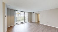 This one-bedroom, one-bathroom unit at 301 Green St in Portsmouth, Virginia, offers a thoughtfully arranged single-level layout that maximizes its compact footprint. The living room serves as the heart of the space, distinguished by expansive floor-to-ceiling windows dressed with vertical blinds that flood the room with natural light and provide views of the surrounding greenery. Light wood-tone flooring runs throughout the living and common areas, contributing to a clean, cohesive aesthetic, while a pendant light fixture adds a modern accent overhead.

The kitchen is efficiently designed with white shaker-style cabinetry, light quartz countertops, a stainless steel refrigerator, and a gas range, offering functional workspace despite its compact size. Wood-look tile flooring carries through this area seamlessly. A hallway connects the main living spaces to the private areas of the unit, including a dedicated closet for storage.

The bedroom features neutral carpet flooring and a window allowing natural light to enter, creating a calm and restful atmosphere. The bathroom is clean and bright, outfitted with a white vanity, a mirrored medicine cabinet, tile surround, and a shower-tub combination. Neutral tones throughout the unit lend a versatile, move-in-ready ambiance.