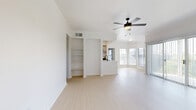 This single-floor, 3-bedroom, 2-bathroom residence in Austin, TX offers a well-designed open-concept layout finished in a bright, neutral palette throughout. The combined living and kitchen area forms the heart of the home, where light wood-look flooring, crown molding, and a ceiling fan with light fixture create an airy, cohesive atmosphere. A wall of windows and sliding glass doors with vertical blinds floods the living area with natural light. The kitchen features a white peninsula island with a matte black sink faucet, white cabinetry, stainless steel appliances including a refrigerator and range, and open shelving — all flowing seamlessly into the living space. A built-in shelving unit provides additional storage in the main living area. The three bedrooms include a well-proportioned primary suite with light wood flooring, built-in shelving, and access to its own bathroom. The primary bathroom is a standout, boasting a glass-enclosed walk-in shower with floor-to-ceiling marble-style tile, a white vanity with matte black hardware, and light wood flooring. Secondary bedrooms feature plush carpet flooring and ceiling fans, with one offering a bright window view to the outdoors. Two carpeted walk-in closets with wire shelving provide ample storage throughout the home.