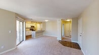 This single-floor residence features an open-concept design that seamlessly connects the living, dining, and kitchen areas. The living room is carpeted and anchored by a fireplace, with large windows and sliding glass doors that lead to a private balcony, filling the space with natural light and outdoor views. The kitchen is well-appointed with white cabinetry featuring modern hardware, granite countertops, a subway tile backsplash, and stainless steel appliances including a range, over-the-range microwave, and dishwasher. A peninsula with a stainless steel sink and additional counter space provides a natural divide between the kitchen and living areas. Track lighting illuminates the kitchen efficiently. Wood-look flooring runs through the kitchen and entry areas, transitioning to plush carpet in the living spaces. A hallway leads to additional rooms, including a bathroom outfitted with granite countertops, an undermount sink, white cabinetry, and a large mirror. The entry door area transitions smoothly between hard flooring and carpet, reinforcing the functional layout. Neutral wall tones and consistent finishes throughout contribute to a cohesive, move-in-ready aesthetic.