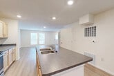 This two-story home is thoughtfully laid out across two equally sized floors, offering a practical and comfortable living environment. The main level features an open-concept living and kitchen area, where light-toned laminate flooring flows seamlessly throughout. The kitchen is equipped with stainless steel appliances, including an electric range, over-the-range microwave, and refrigerator, complemented by light wood cabinetry and gray laminate countertops. A peninsula with a double-basin sink connects the kitchen to the living area, making it ideal for everyday functionality. Large windows allow natural light to fill the living room, which also includes a welcoming front entry door. Upstairs, three bedrooms are finished with plush wall-to-wall carpeting and feature windows that bring in additional natural light. The primary bedroom is generously sized and includes access to a dedicated walk-in closet outfitted with wire shelving along multiple walls. The bathrooms are finished in a clean, modern style, featuring light wood vanities, white countertops, and large frameless mirrors. A hallway and two staircases ensure smooth circulation between floors. Neutral warm tones and consistent finishes throughout give the home a cohesive, move-in-ready feel.