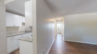 This single-floor unit offers a clean, functional layout designed for comfortable everyday living. Rich wood-look flooring runs consistently throughout the space, providing a warm, cohesive aesthetic that ties each room together. A central hallway connects the main living areas, creating a logical and efficient flow from room to room.

The galley-style kitchen is a standout feature, outfitted with crisp white shaker cabinetry, granite countertops, an undermount sink with a modern faucet, and white appliances including a coil-burner range with overhead exhaust and a full-size refrigerator. The kitchen's thoughtful layout maximizes storage and prep space along both walls.

The living area is generously proportioned, bathed in natural light from a large window fitted with a window A/C unit, and finished with neutral-toned walls and a textured ceiling. An additional room, suitable as a bedroom or flex space, offers a notable highlight — a window framing a picturesque water view with lush greenery beyond, filling the room with natural light and a tranquil outlook.

The bathroom features a full tub-shower combination with classic white subway tile surround, a granite-topped vanity, and clean white fixtures throughout, maintaining the unit's consistent, updated aesthetic. White trim and neutral wall tones unify the entire space.