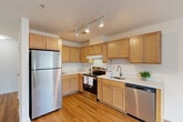 Located at 7053 Spring Pl NW in Washington, DC, this one-bedroom, one-bathroom residence offers a thoughtfully organized layout across a single floor. The open-concept living, dining, and kitchen area forms the heart of the home, with warm hardwood flooring flowing throughout. The kitchen is well-appointed with light maple cabinetry offering generous storage, stainless steel appliances including a full-size refrigerator, electric range, and dishwasher, complemented by white countertops and track lighting overhead. The seamless connection between the kitchen and living and dining areas creates a functional, cohesive space for everyday living. Two hallways connect the main living area to the private quarters, with four closets distributed throughout the unit providing exceptional storage capacity for a residence of this size. The bedroom features soft carpeting, a window allowing natural light to filter in, and direct closet access. The bathroom is clean and functional, finished with white tile flooring, a shower/tub combination, and a wood-toned vanity with ample counter space. The overall design is clean and neutral, with white walls and consistent finishes creating a bright, move-in-ready environment throughout.
