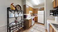 This single-floor residence offers a cohesive and comfortable layout designed for everyday living. The kitchen features warm wood cabinetry, a white electric range, a full-size refrigerator, and light hardwood-style flooring, complemented by a decorative open shelving unit that adds character to the space. Adjacent to the kitchen, the dining area accommodates a full dining table set beneath a large framed mirror that adds depth and visual interest, with built-in wall shelving providing additional display space. The living room is carpeted and inviting, with a textured ceiling, a ceiling light fixture, and ample room for seating arrangements. Two bedrooms are both carpeted and feature ceiling fans with light fixtures and window blinds that allow for natural light control. The primary bedroom includes generous dresser storage and framed wall art, while the secondary bedroom has a cozy, well-defined layout with a windowed wall. Both bathrooms are finished with warm wood vanity cabinetry, white countertops, hardwood-style flooring, and framed mirrors above the sinks. One bathroom includes a shower-tub combination with a decorative curtain. Throughout the home, neutral wall tones and textured ceilings provide a consistent, understated backdrop that ties each room together.