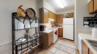 This single-floor residence offers a cohesive and comfortable layout designed for everyday living. The kitchen features warm wood cabinetry, a white electric range, a full-size refrigerator, and light hardwood-style flooring, complemented by a decorative open shelving unit that adds character to the space. Adjacent to the kitchen, the dining area accommodates a full dining table set beneath a large framed mirror that adds depth and visual interest, with built-in wall shelving providing additional display space. The living room is carpeted and inviting, with a textured ceiling, a ceiling light fixture, and ample room for seating arrangements. Two bedrooms are both carpeted and feature ceiling fans with light fixtures and window blinds that allow for natural light control. The primary bedroom includes generous dresser storage and framed wall art, while the secondary bedroom has a cozy, well-defined layout with a windowed wall. Both bathrooms are finished with warm wood vanity cabinetry, white countertops, hardwood-style flooring, and framed mirrors above the sinks. One bathroom includes a shower-tub combination with a decorative curtain. Throughout the home, neutral wall tones and textured ceilings provide a consistent, understated backdrop that ties each room together.