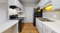 Located at 215 N Baird Ln in Murfreesboro, Tennessee, this single-floor, one-bedroom, one-bathroom unit offers a practical and well-organized layout. The galley-style kitchen is a standout feature, equipped with ample white cabinetry both above and below the counters, a light-toned quartz-style countertop, a stainless steel sink, a black electric range with overhead ventilation, and a black refrigerator. Warm wood-look flooring runs through the kitchen, adding a welcoming contrast to the bright white cabinetry. A closet at the end of the kitchen provides additional storage. The bedroom is comfortably sized, finished with soft wall-to-wall carpeting in a neutral tone and painted in a calm gray. A window allows natural light to filter in, and a private door leads to additional storage or closet space. The bathroom is clean and straightforward, featuring a full tub-shower combo with chrome fixtures, a toilet, and matching wood-look flooring that ties the space together. A hallway connects the rooms efficiently, contributing to the unit's smart use of space. Overall, the unit presents a neutral, move-in-ready palette with consistent finishes throughout.