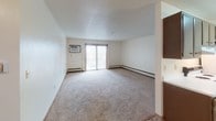 Located at 400 S Sneve Ave in Sioux Falls, South Dakota, this single-floor unit offers a practical and comfortable layout designed for everyday living. The open living area is finished with neutral carpet and textured ceilings, and features a ceiling fan with integrated lighting. Baseboard heating runs along the perimeter of the main living space, which is anchored by a wall-mounted air conditioning unit and a sliding glass door that opens to a private balcony, allowing natural light to filter in. The transition between the carpeted living area and the tiled entryway/kitchen zone creates a clear distinction between spaces within the open floor plan. The kitchen area connects seamlessly to the main living space, as seen in the overhead floor plan view, which also reveals additional storage and cabinetry along the corridor. The bedrooms are generously proportioned, each equipped with ceiling fans, soft carpet underfoot, and windows that frame outdoor views of surrounding trees, enhancing the sense of openness. Baseboard heaters are present in the bedrooms as well, ensuring consistent warmth throughout. The bathroom features a full tub-shower combo with white tile surround, a toilet, vanity with sink, and chrome hardware and towel bar, offering a clean and functional design. Overall, the unit presents a straightforward, well-maintained living environment in a residential Sioux Falls neighborhood.