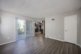 Located at 6575 Jaffe Court in San Diego, CA, this efficiently designed single-floor unit makes smart use of its compact footprint. Wood-look flooring runs throughout the main living areas, complementing neutral gray walls and textured ceilings for a clean, cohesive aesthetic.

The living room is bright and open, featuring a ceiling fan, a wall-mounted air conditioning unit, and a sliding glass door dressed with vertical blinds that leads directly to the private patio. Greenery visible through the windows and patio door adds a touch of the outdoors to the living space.

The kitchen is a standout feature, designed in a galley style with dark wood-toned cabinetry on both sides, white quartz countertops, and a full suite of stainless steel appliances including a range, over-the-range microwave, and refrigerator. A peninsula counter connects the kitchen to the dining area, creating a natural flow between the two spaces. A ceiling fan overhead keeps the area comfortable.

Two closets provide practical storage solutions throughout the unit. The bathrooms are clean and functional, featuring a shower/tub combo with a curved curtain rod and chrome fixtures.

The private patio offers a pleasant outdoor retreat with views of surrounding greenery, rounding out this well-appointed San Diego residence.