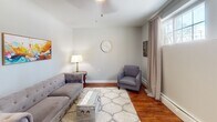 Located at 105 N Willow St in Liverpool, NY, this 2-bedroom, 1-bathroom single-floor residence offers a practical and comfortable layout with consistent design details throughout. Warm hardwood flooring runs through the main living areas and bedrooms, lending a cohesive and inviting feel to the space.

The living room is bright and welcoming, featuring a ceiling fan, large windows dressed with neutral drapes, and a baseboard heating system. Natural light fills the room, creating an airy atmosphere well-suited for relaxing or entertaining.

The kitchen is equipped with dark cabinetry, black appliances including an electric range and over-the-range microwave, a subway tile backsplash, and a window that brings in additional light. Adjacent dining space provides room for a table, keeping everyday living convenient.

Both bedrooms are comfortably scaled, each with windows, ceiling fans, and baseboard heating. The primary bedroom features mirrored sliding closet doors, maximizing the sense of space, while the second bedroom offers its own window and closet access. Two closets serve the unit overall.

The bathroom is clean and well-finished, with tile flooring, a stone-topped vanity with ample cabinetry, and crisp white walls. The overall ambiance of the home is neutral, tidy, and move-in ready, making it a practical option in the Liverpool area.