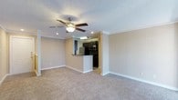 This single-floor space showcases an open-concept design that seamlessly connects the living area to the kitchen. The living room is finished with neutral-toned carpet and warm beige walls, creating a clean and inviting atmosphere. Crown molding lines the ceiling throughout, adding a refined architectural detail, while a ceiling fan with a built-in light fixture provides both comfort and illumination. Recessed lighting further enhances the brightness of the space.

The kitchen is accessible via a raised breakfast bar peninsula, which serves as a natural divider between the two areas. It is outfitted with dark espresso cabinetry and stainless steel appliances, including a refrigerator, microwave, and range, offering a modern contrast to the lighter tones of the living space. The kitchen features tile flooring, distinguishing it from the carpeted living area. A textured popcorn ceiling is present throughout, and white baseboards frame each room, contributing to a cohesive, polished finish. Overall, the layout is functional and well-appointed.