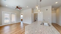 This single-floor unit showcases a thoughtfully designed open-concept layout that seamlessly connects the kitchen, dining, and living areas. Light-toned hardwood-style flooring runs throughout, complementing the neutral warm-beige wall palette and crisp white trim to create a bright, cohesive aesthetic.

The kitchen serves as a focal point, featuring dark espresso cabinetry that extends to the ceiling for generous storage, granite countertops, a herringbone-pattern tile backsplash, and a full suite of stainless steel appliances including a refrigerator, range, and built-in microwave. A large central island with a granite surface and undermount sink is illuminated by a trio of glass pendant lights, making it ideal for both meal prep and casual dining.

The living area benefits from a ceiling fan, recessed lighting, and direct access to an exterior door, allowing natural light to flow freely. A separate bedroom offers a large window with outdoor views, while a spacious walk-in closet provides ample shelving and hanging storage. The bathroom features a subway-tiled tub and shower surround, granite vanity, and dark cabinetry. A hallway pantry tower adds further storage convenience near the kitchen.