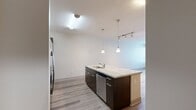 This 710-square-foot, two-bedroom, one-bathroom condo on the 5th floor at 1330 Market St in downtown San Diego offers a well-designed single-level layout with modern finishes throughout. The open-concept kitchen and living area serves as the heart of the unit, featuring a large granite island with a built-in sink, pendant lighting, dark espresso cabinetry with sleek hardware, stainless steel appliances including a refrigerator, range, and microwave, and a tile backsplash. Wood-style plank flooring runs throughout the entire unit, providing a cohesive and contemporary aesthetic. The living room benefits from natural light via large windows and a glass door that opens to an outdoor area. Both bedrooms are equipped with ceiling fans and are connected to the shared hallway, with the primary bedroom spanning 140 square feet and offering direct access to the bathroom. The full bathroom includes a soaking tub, a separate tiled shower, a dual-sink vanity with dark cabinetry, a large mirror with overhead lighting, and tile flooring. A dedicated closet provides additional storage. Track lighting and recessed fixtures add to the unit's clean, modern ambiance.