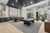 Imagine unwinding in a space where soaring ceilings, floor-to-ceiling black-framed windows, and breathtaking pool views set the tone for elevated everyday living. This 800 sq ft showpiece lounge at Riverwood features a sleek pool table, a wall-mounted large-screen TV, and chic blue cabinetry with designer pendant lighting. Plush banquette seating, curated lounge chairs, and light hardwood floors create an ambiance that's both vibrant and refined. This is the lifestyle you've been dreaming of — yours to enjoy in Raleigh, NC.
