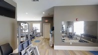Located at 3400 Briarcliff Rd in Greenville, NC, this fitness center offers a well-equipped, single-floor workout facility designed to support a full range of exercise routines. The space features a clean, modern interior with neutral gray walls, recessed lighting, and light-toned striped flooring that contributes to a bright and energizing atmosphere. Large windows along the perimeter allow natural light to fill the room, enhancing the open feel of the space. The facility is outfitted with a variety of cardio machines, including treadmills and ellipticals, positioned to take advantage of the natural light. Strength training equipment is also available throughout the space, providing options for both machine-based and free-movement workouts. A floor-to-ceiling mirror is mounted on one wall, a practical feature that allows users to monitor their form during exercise. A water dispenser is conveniently located within the space for easy access during workouts. The layout is thoughtfully organized to maximize usable floor space, ensuring a comfortable and functional environment. The overall ambiance is clean, orderly, and welcoming, making it a practical and well-maintained facility suited for everyday fitness use.