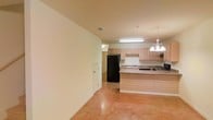 Located at 26676 Canal Rd. in Orange Beach, Alabama, this two-story property offers a practical and functional layout suited for coastal living. The open-concept main level seamlessly connects the kitchen and living areas, creating a spacious, airy feel throughout. The kitchen is equipped with light wood cabinetry, a kitchen island with a breakfast bar overhang, a double sink, and full-size appliances including a refrigerator and range. A chandelier-style pendant light adds a decorative touch above the island, complementing the overhead fluorescent lighting that brightens the workspace. The flooring throughout the main level features polished concrete with warm, earthy tones, lending the space an industrial yet inviting character. Neutral-toned walls keep the interior bright and versatile. Recessed HVAC vents are integrated into the ceiling, ensuring year-round comfort. A interior door off the kitchen provides access to additional rooms or utility areas. With two full floors, this property offers ample room for living, storage, or additional accommodations, making it a well-rounded option in the Orange Beach area.