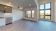 Located at 1707 N Main St in Walnut Creek, California, this single-floor unit offers a contemporary design with clean lines and high-quality finishes throughout. The open living area is bright and airy, featuring light wood-style flooring, crisp white walls, and recessed lighting. Large black-framed windows allow generous natural light to fill the space and provide treetop views, while a private balcony access adds an outdoor connection to the living area.

The kitchen is thoughtfully designed with two-tone cabinetry — glossy upper cabinets in a warm gray paired with white lower cabinets — complemented by a decorative stone-pattern backsplash and light countertops. A full suite of stainless steel appliances, including a French door refrigerator, electric range, built-in microwave, and dishwasher, rounds out this functional and stylish space.

The bedroom area offers ample room with the same light flooring and access to a well-organized closet. The bathroom is a standout feature, finished with large-format tile flooring and a walk-in glass-enclosed shower adorned with striking marble-style tile from floor to ceiling, creating a clean, spa-like aesthetic. White cabinetry provides convenient storage. Overall, the unit presents a modern, move-in-ready environment in a desirable Walnut Creek location.