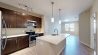 This thoughtfully designed one-bedroom, one-bathroom residence offers a functional and modern living experience across a single floor. The open-concept kitchen and living area forms the heart of the home, anchored by a large center island with a white quartz countertop, an integrated sink, and stylish pendant lighting above. Dark espresso cabinetry lines the kitchen walls, complemented by a subway tile backsplash, stainless steel appliances — including a range, microwave, and refrigerator — and ample storage. Light wood-style flooring extends throughout the main living areas, creating a warm, cohesive aesthetic. Natural light filters in through windows in the living area, contributing to an airy, open ambiance. The bedroom is a comfortable retreat featuring plush carpeting, a ceiling fan, and a window with exterior views. It connects directly to a dedicated closet and the full bathroom, which includes a tub-shower combination with white tile surround, wood-style flooring, and a vanity with dark cabinetry. Clean, neutral wall tones throughout the space provide a versatile backdrop, making the residence move-in ready and easy to personalize.