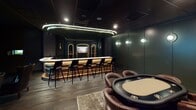 This single-level entertainment space is thoughtfully designed to deliver an immersive, upscale lounge experience across several distinct zones. The centerpiece is a curved full-service bar finished with an illuminated stone countertop and warm wood paneling, complemented by a row of sleek black barstools. Arched backbar cabinetry and globe wall sconces against deep forest-green paneled walls lend a refined, speakeasy-inspired character. A dropped black tile ceiling with recessed and neon accent lighting reinforces the intimate, dramatic atmosphere throughout.

Adjacent to the bar area is a dedicated poker room, where a large oval poker table surrounded by tufted brown leather chairs sits beneath recessed ceiling lights. Textured gray wall panels and a wall-mounted flat-screen television complete this focused gaming environment. Nearby, a high-definition golf simulator occupies its own darkened bay, featuring a full projection screen, astroturf hitting mat, overhead projector, and comfortable seating for spectators. Dark draping curtains frame the simulator screen, enhancing focus and visual contrast. Rich hardwood flooring flows throughout, unifying all areas into a cohesive, sophisticated entertainment suite.