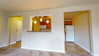 This single-floor residence offers a practical and well-organized layout across several distinct living spaces. The entry welcomes you with durable tile flooring that extends into the kitchen, providing a clean transition into the home. The living area is generously sized, featuring wall-to-wall neutral carpet, warm beige walls, and baseboard heating running along the perimeter. Natural light filters in through windows fitted with blinds, giving the space a bright, open feel. A pass-through window with a granite-style counter connects the living area to the kitchen, which is equipped with warm oak cabinetry, dark countertops, a full suite of white appliances including a refrigerator, dishwasher, electric range, and built-in microwave, and overhead pendant lighting. Two carpeted bedrooms each include a window with outdoor views, baseboard heating, and a window air conditioning unit in one room, offering comfortable, functional retreats. The bathroom features full white tile surround around the soaking tub, tile flooring, and clean white fixtures throughout. The overall ambiance is practical and neutral, offering a move-in-ready environment.