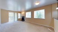 This single-floor residence offers a well-designed layout with a cohesive, neutral color palette of warm beige tones throughout. The expansive living room serves as the centerpiece of the home, featuring plush wall-to-wall carpeting, a sleek black fireplace, and an abundance of natural light streaming through multiple large windows and a sliding glass door that opens to an outdoor balcony, offering views of lush greenery. The open layout provides generous space for a variety of furniture arrangements.

The kitchen is thoughtfully designed with light maple cabinetry, dark granite-style countertops, and a full suite of stainless steel appliances including a refrigerator, electric range, over-the-range microwave, and dishwasher. Durable slate-style tile flooring adds a practical and stylish touch, and a pendant light fixture illuminates the workspace. A back door with a window provides additional natural light.

The two bedrooms are carpeted and feature double-door closets, windows for natural light, and baseboard heating. One bedroom benefits from a larger window with an outdoor view. The full bathroom is finished with wood-look plank flooring, a single-sink vanity with light maple cabinetry, and a tub-shower combination. A separate entry area with tile flooring connects the kitchen to the front door, completing this functional and comfortable home.