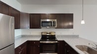 This single-floor unit is designed with a functional and cohesive aesthetic throughout. The kitchen serves as a standout feature, showcasing rich dark-espresso cabinetry with brushed nickel hardware, granite-style speckled countertops, and a full suite of stainless steel appliances including an electric range, over-the-range microwave, and refrigerator. A peninsula with an undermount sink and pendant lighting overhead adds both workspace and visual appeal, while dark hardwood-style flooring grounds the space with warmth and contrast.

The living areas are finished with neutral wall-to-wall carpeting and bright white walls, creating a clean, airy atmosphere. Ceiling fans with integrated lighting are present throughout, contributing to both comfort and functionality. Natural light filters in generously through windows fitted with horizontal blinds.

The unit includes multiple bedrooms, each spacious and well-lit with natural light. The bathrooms offer practical, clean finishes—one features a full soaking tub and shower combination with a pedestal sink, while another includes a standalone walk-in shower with sliding glass doors and a dark-cabineted vanity with matching granite-style countertop. Hardwood-style flooring carries through the bathrooms, maintaining a consistent design language throughout the unit.