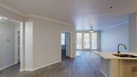 This single-floor residence offers a thoughtfully designed layout that balances comfort and functionality throughout. The open-concept living and dining area is finished with wood-look flooring, crown molding, and a ceiling fan with light fixture. Large French doors flood the space with natural light and open directly onto a private balcony, providing pleasant outdoor views. The kitchen is equipped with stainless steel appliances, including an electric range, microwave, and refrigerator, complemented by white cabinetry, a subway tile backsplash, and a light quartz peninsula with an integrated sink — ideal for both everyday cooking and casual dining. The entry foyer provides a welcoming transition into the main living spaces, with flush-mount lighting overhead. The bedrooms feature plush wall-to-wall carpeting and well-sized windows dressed with blinds that allow for natural light and privacy. One bedroom benefits from a generously sized walk-in closet outfitted with multi-tiered wire shelving on three walls, offering abundant storage. Throughout, the space is painted in a soft neutral palette, with consistent crown molding and clean white baseboards tying each room together for a cohesive and polished aesthetic.