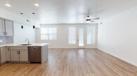 This well-designed single-floor residence offers a clean, modern aesthetic throughout its open and thoughtfully arranged layout. The heart of the home is a spacious open-concept living and kitchen area united by light-toned wood-style flooring that extends seamlessly across the main space. The kitchen is outfitted with stainless steel appliances — including a range, over-the-range microwave, dishwasher, and refrigerator — complemented by grey shaker-style cabinetry, a grey subway tile backsplash, and a generous island with a white countertop and an undermount sink. Sleek pendant lighting hangs above the island, adding a contemporary touch. The living area is bright and airy, benefiting from multiple windows with blinds and a glass-paneled exterior door that invites natural light throughout. A ceiling fan serves the main living space for year-round comfort. The bathroom features matching grey cabinetry with black hardware, a wide vanity with a light countertop, a large mirror, and wood-style flooring. The bedroom is a tranquil retreat with soft carpet, corner windows providing ample natural light, and crisp white walls. Throughout, the space maintains a cohesive, neutral palette that is both inviting and move-in ready.