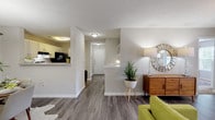 Located at 100 Camellia Ln in Lithonia, Georgia, this well-appointed single-floor residence offers a thoughtfully designed layout with a warm, contemporary aesthetic. The open-concept living area features durable wood-look flooring, a ceiling fan, and large windows that invite natural light and views of the surrounding greenery. The adjoining dining space is defined by a pendant light fixture overhead and wood-look flooring that flows seamlessly throughout the common areas. The kitchen is equipped with white cabinetry, black appliances including a gas range and refrigerator, a dishwasher, and light countertops — offering a clean, functional workspace. A pass-through counter connects the kitchen to the main living area, enhancing the open feel. The bedrooms are carpeted for comfort, with the primary suite featuring a walk-in closet and a dedicated en-suite bathroom complete with a wide vanity, large mirror, and abundant lighting. A second bedroom also includes walk-in closet access. The primary bathroom's layout is flanked by closets on either side, providing generous storage. Neutral tones, textured ceilings, and consistent finishes throughout create a cohesive and inviting atmosphere across every room of this single-level home.