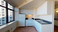 Located at 201 Yesler Way in Seattle's vibrant Pioneer Square district, Unit 1009 is a thoughtfully laid-out single-floor residence that combines functional design with urban convenience. The kitchen is a standout feature, equipped with white cabinetry extending to the ceiling for generous storage, dark countertops, a white electric range, a full-size refrigerator, and a double sink — all complemented by a large window that floods the space with natural light and frames views of the surrounding cityscape. Wood-look flooring runs consistently throughout the unit, lending warmth and visual continuity from room to room. A well-proportioned bedroom includes an open closet with a built-in rod, offering practical storage solutions, and is accented by a wall-mounted sconce. The bathroom features a dark countertop vanity, a toilet, and a towel bar, maintaining the same clean, neutral palette found throughout the unit. A narrow entryway corridor with a wall sconce and electrical panel provides a clear transition into the main living areas. The overall aesthetic is clean and neutral, making the space highly adaptable to a variety of interior styles. Its location in Pioneer Square places residents steps from Seattle's waterfront, dining, transit, and cultural landmarks.