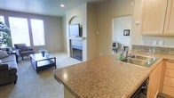 This two-story residence offers a thoughtfully designed open-concept layout that seamlessly connects the kitchen and living areas. The kitchen features polished granite countertops with warm, earthy tones and an integrated sink, providing both functionality and visual appeal. The peninsula-style counter serves as a natural divider between the kitchen and the living space, enhancing the open flow of the main floor.

The living room is finished with neutral-toned carpet and painted in warm beige tones, creating a welcoming atmosphere. A standout feature is the fireplace, framed by a classic white mantle, which anchors the room. Directly above, a decorative arched wall niche adds architectural character and serves as a natural display or media area. Recessed lighting and a window along the side wall bring in natural light, keeping the space bright and airy.

An adjacent room, visible through a doorway, suggests additional flexible living or dining space. The neutral color palette and consistent finishes throughout the main level create a cohesive, move-in-ready environment. The two-story configuration provides additional living or sleeping quarters on the upper level.