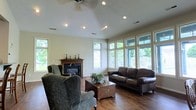 Located at 3995 Cracker Cover Ln in Canal Winchester, Ohio, this single-story home offers a thoughtfully designed layout that balances comfort and functionality. The living room serves as the heart of the home, showcasing vaulted ceilings accented by recessed lighting and a ceiling fan, which together create a sense of openness and airiness. Rich hardwood flooring runs throughout, adding warmth and a timeless aesthetic to the space. A classic fireplace with an elegant dark marble surround and a traditional wood mantel anchors one wall, providing a cozy focal point for the room. An expansive bank of large windows lines the opposite side of the living area, flooding the space with natural light and offering pleasant views of the surrounding outdoor landscape, including a glimpsed deck or patio area and lush greenery beyond. The neutral wall palette and bright trim work complement the natural tones of the flooring and furnishings seamlessly. The overall ambiance of this home is warm, inviting, and well-lit, with architectural details that elevate everyday living. The single-floor layout ensures ease of movement throughout, making this Canal Winchester property a comfortable and practical place to call home.